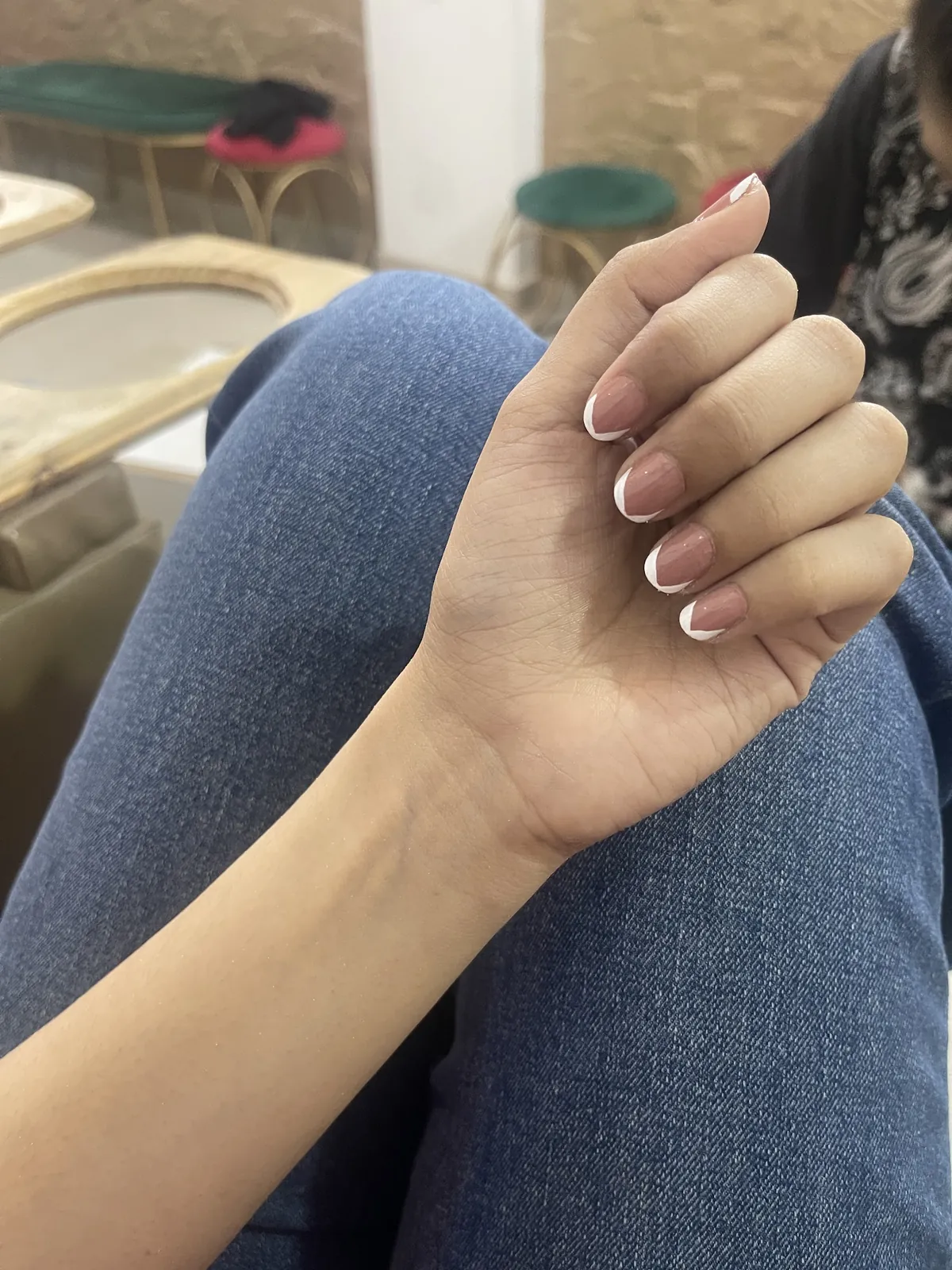 A client's fresh French manicure inside the salon, with gold-framed chairs and green velvet stools behind